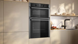 Neff N50 U1ACE2AN3B Built-in Electric Double Oven in Stainless Steel - A/B Rated by HomeWise Appliances. Stock photo showing oven in a kitchen setting.